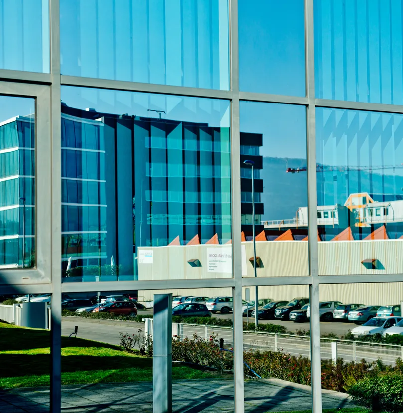 Façade vitrée d'un bâtiment moderne reflétant un immeuble voisin et un parking — zone ZIPLO