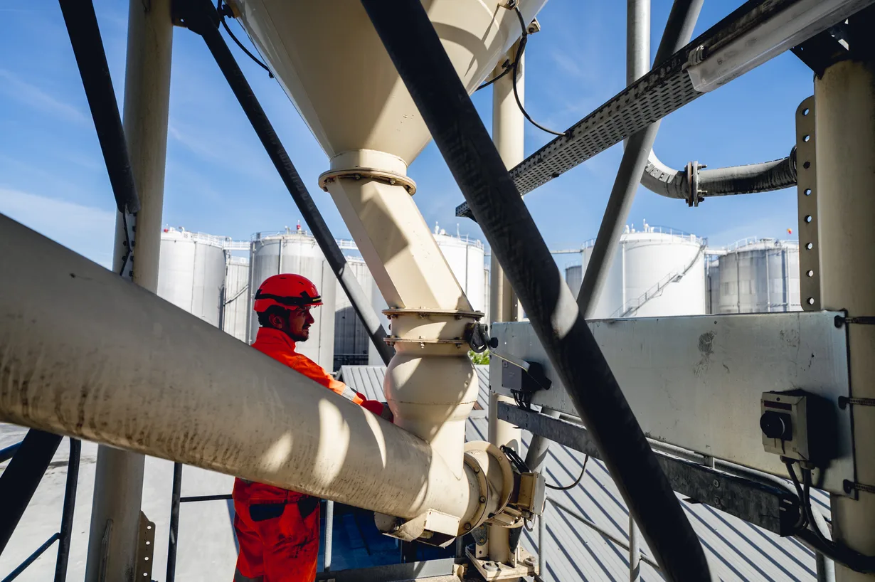 Ouvrier en tenue de sécurité parmi les canalisations et réservoirs d'un dépôt pétrolier