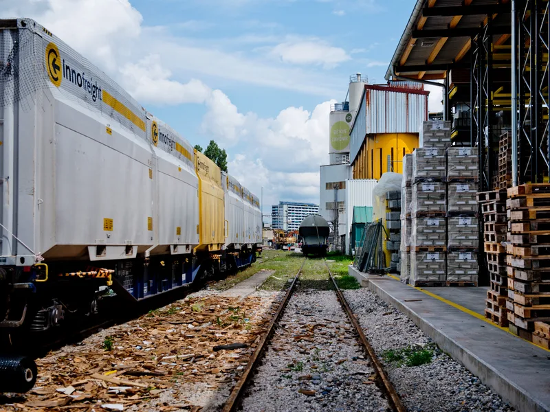 Wagons de fret sur voie ferrée le long d'un bâtiment industriel, avec palettes stockées