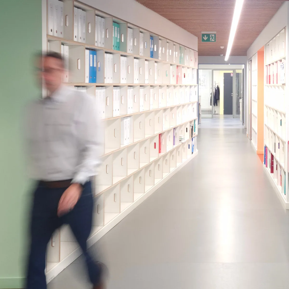 Collaborateur marchant dans un couloir bordé d'étagères d'archives, dans les bureaux de la FTI