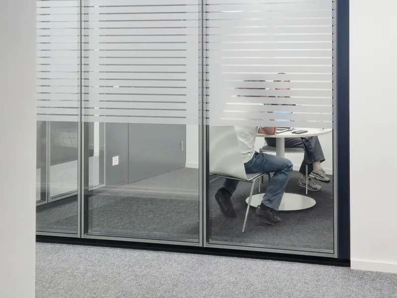 Salle de réunion vitrée où une personne est assise à une table, dans les bureaux de la FTI