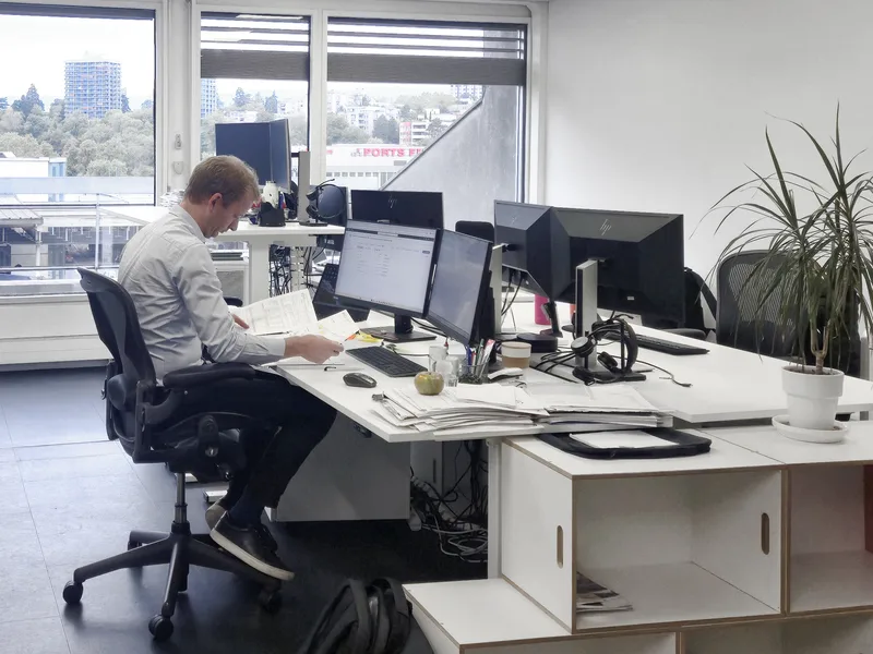 Collaborateur à son poste de travail devant deux écrans, en open space avec vue sur la ville