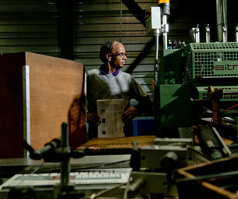 Ouvrier dans un atelier d'imprimerie tenant un journal, devant des presses